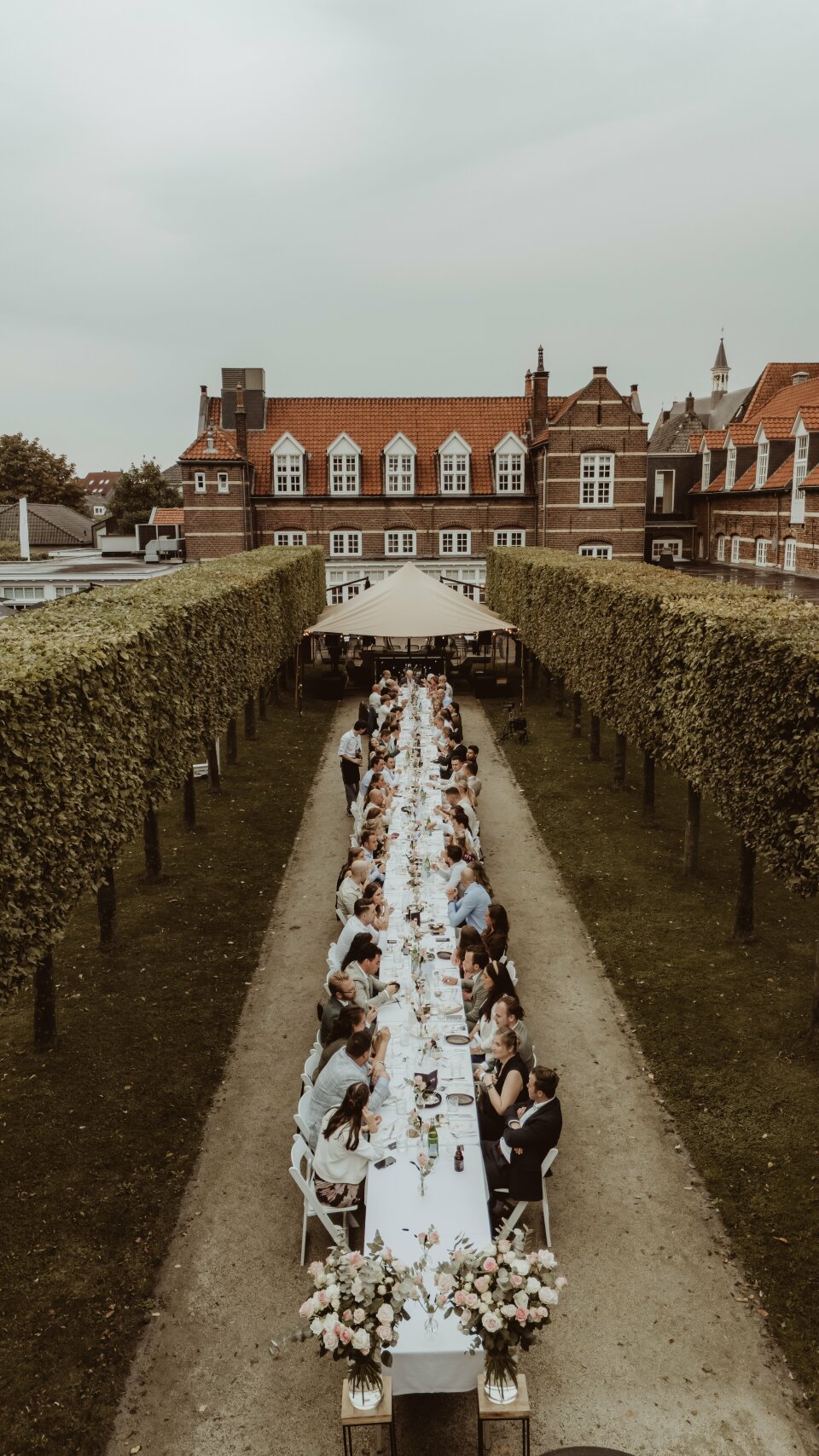 een groep mensen die aan een lange tafel zitten in het midden van een tuin