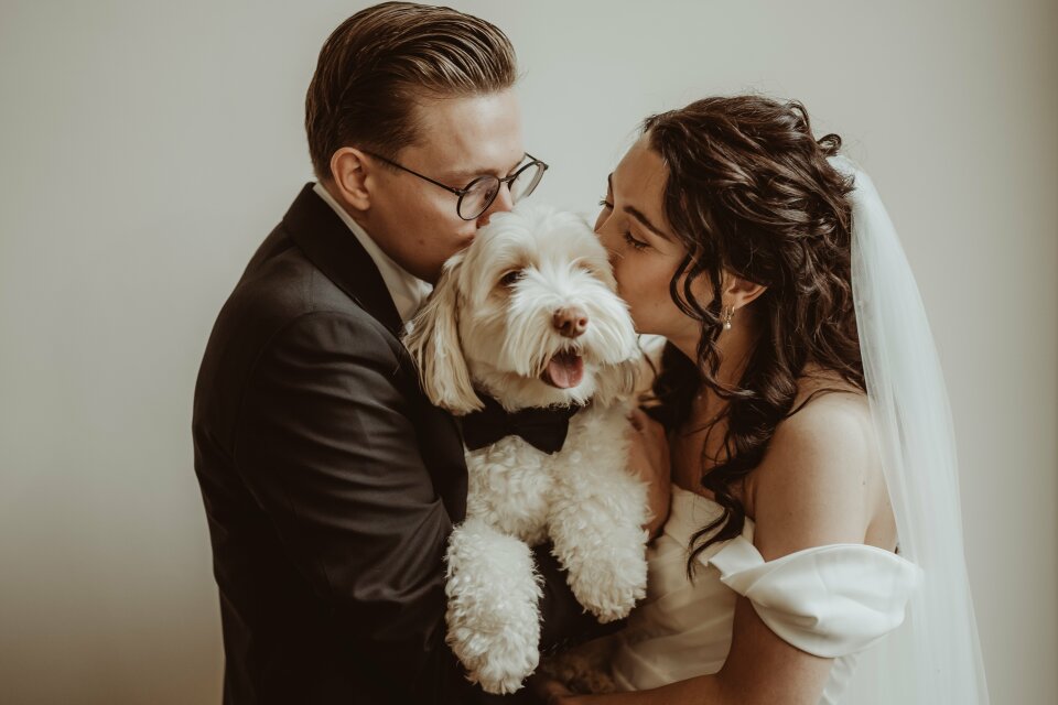 een afbeelding van een bruid en bruidegom die hun hond kussen