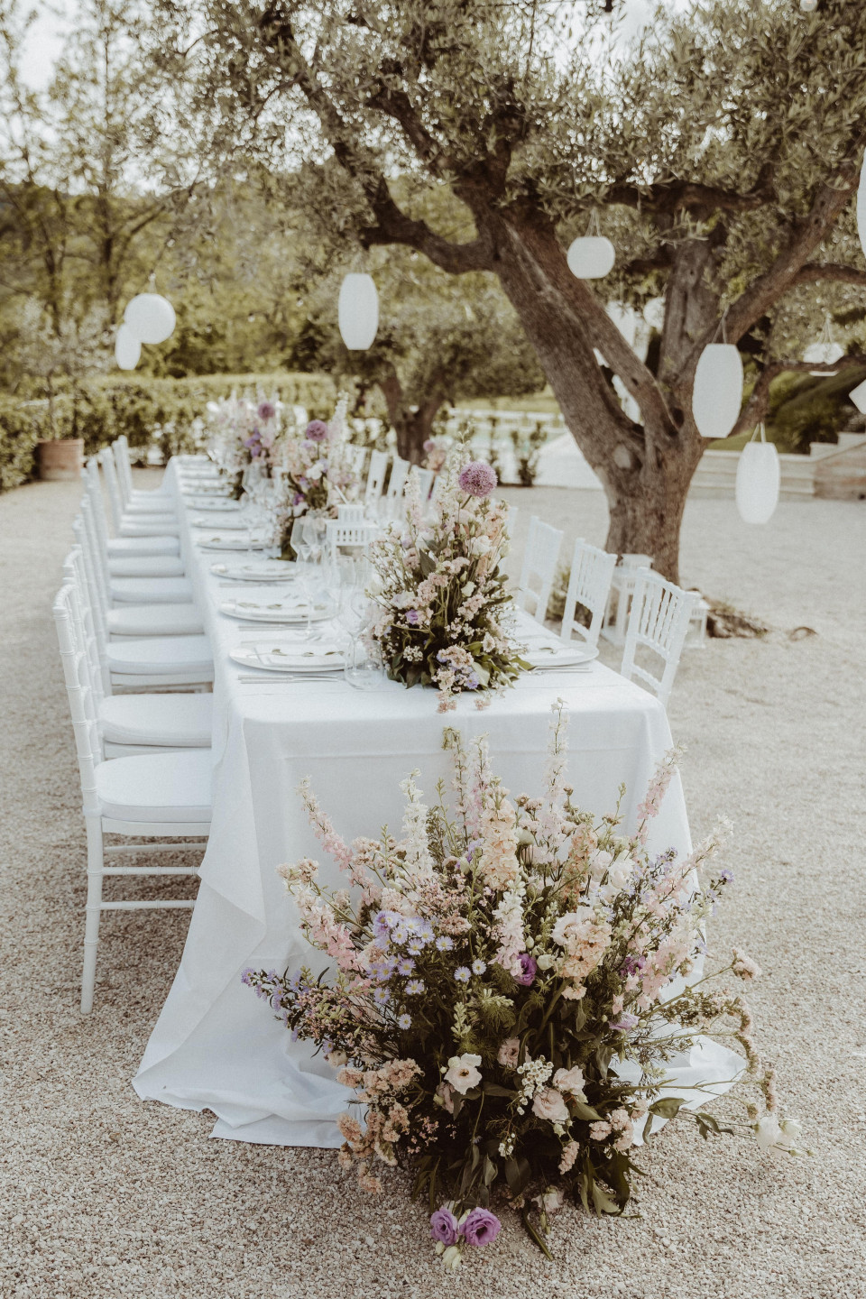 een lange tafel met witte stoelen en bloemen