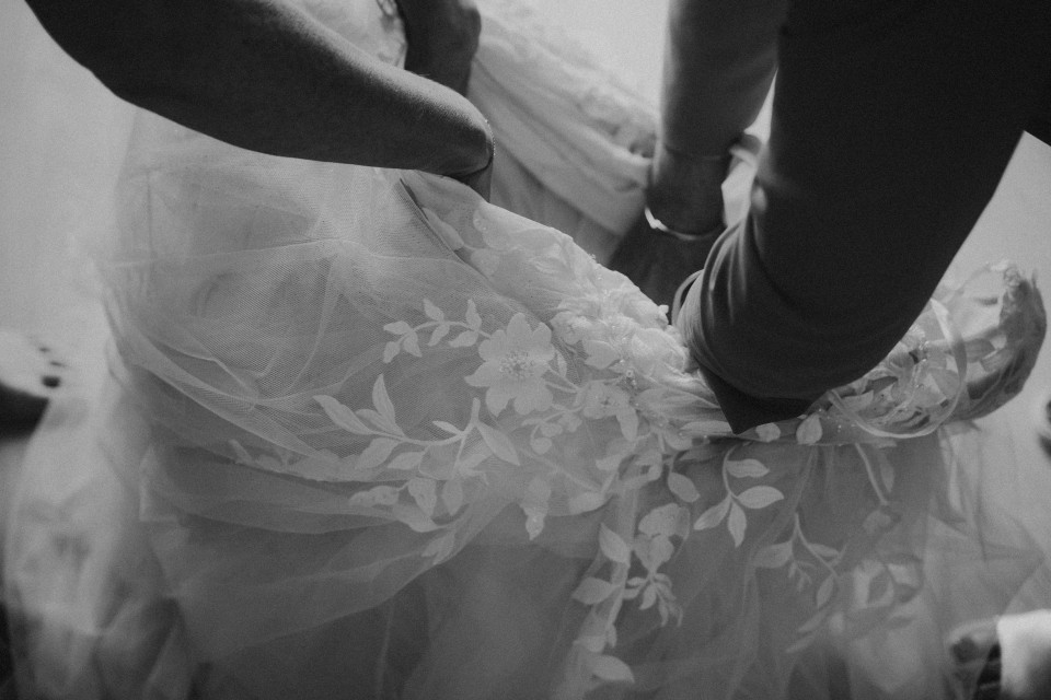 een zwart-wit foto van een bruid die haar trouwjurk aantrekt