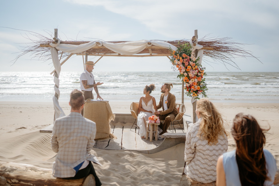 een huwelijksceremonie op het strand met een stel en hun gasten