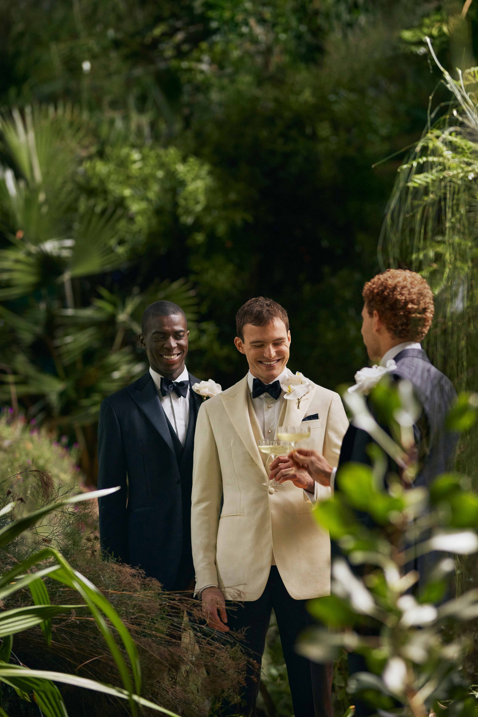 drie mannen in smokings staan in een tropische tuin