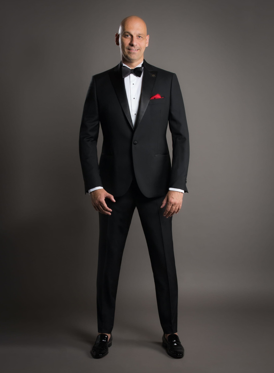 een kale man in smoking die poseert voor de camera